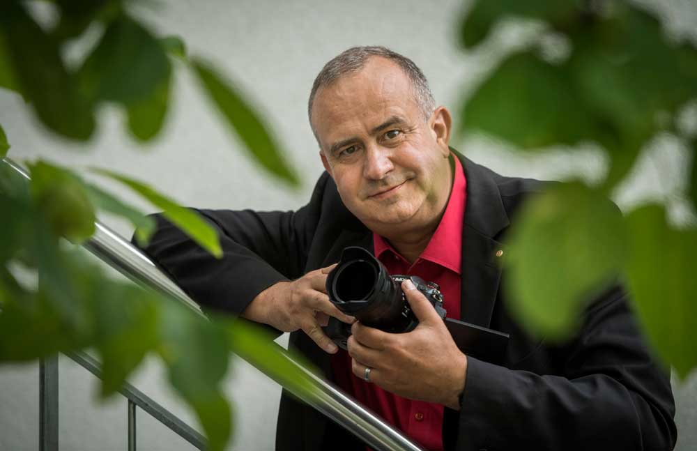 Daniel Felix lehnt an einem Treppengeländer und hält eine Kamera in der Hand